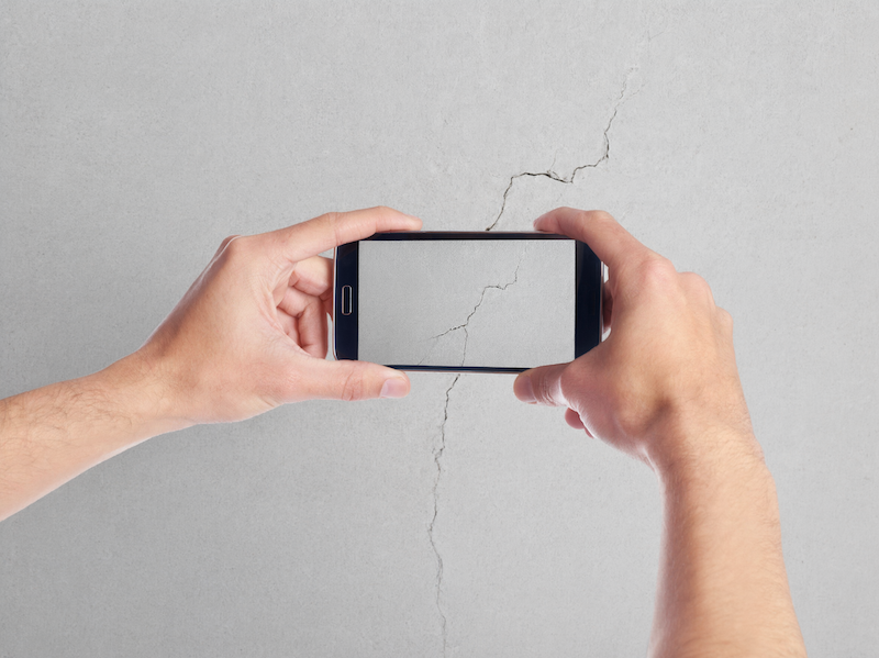 Osoba mobitelom fotografira pukotinu na zidu kako bi dokumentirala postojeće oštećenje u stanu.