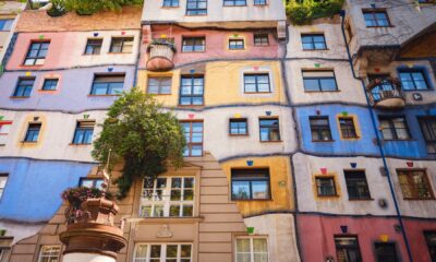 Šareno pročelje Hundertwasserove kuće u Beču s valovitim plohama u ružičastoj, plavoj i žutoj boji, prozorima različitih oblika i zelenilom na pročelju