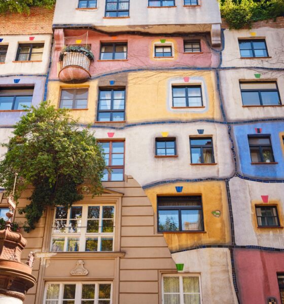 Šareno pročelje Hundertwasserove kuće u Beču s valovitim plohama u ružičastoj, plavoj i žutoj boji, prozorima različitih oblika i zelenilom na pročelju